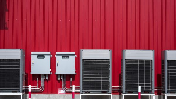 Row of air conditioner compressors with 2 electric control cabinets and electric pipelines system on red metal sheet wall outside of building in Waverly FL