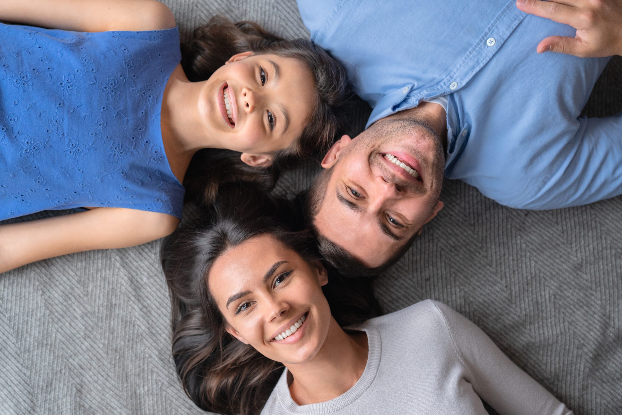 Happy family concept. Top view of happy family of three bonding to each other and smiling while lying on the floor