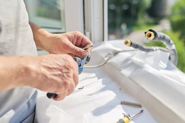 Installing an air conditioner in an apartment office, close-up of an engineer installer's hands working with an outdoor unit, male technician repairing with tools in Waverly FL