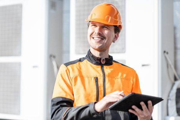 Portrait of a professional workman in protective clothing adjusting the outdoor unit of the air conditioner or heat pump with digital tablet in Bartow, FL