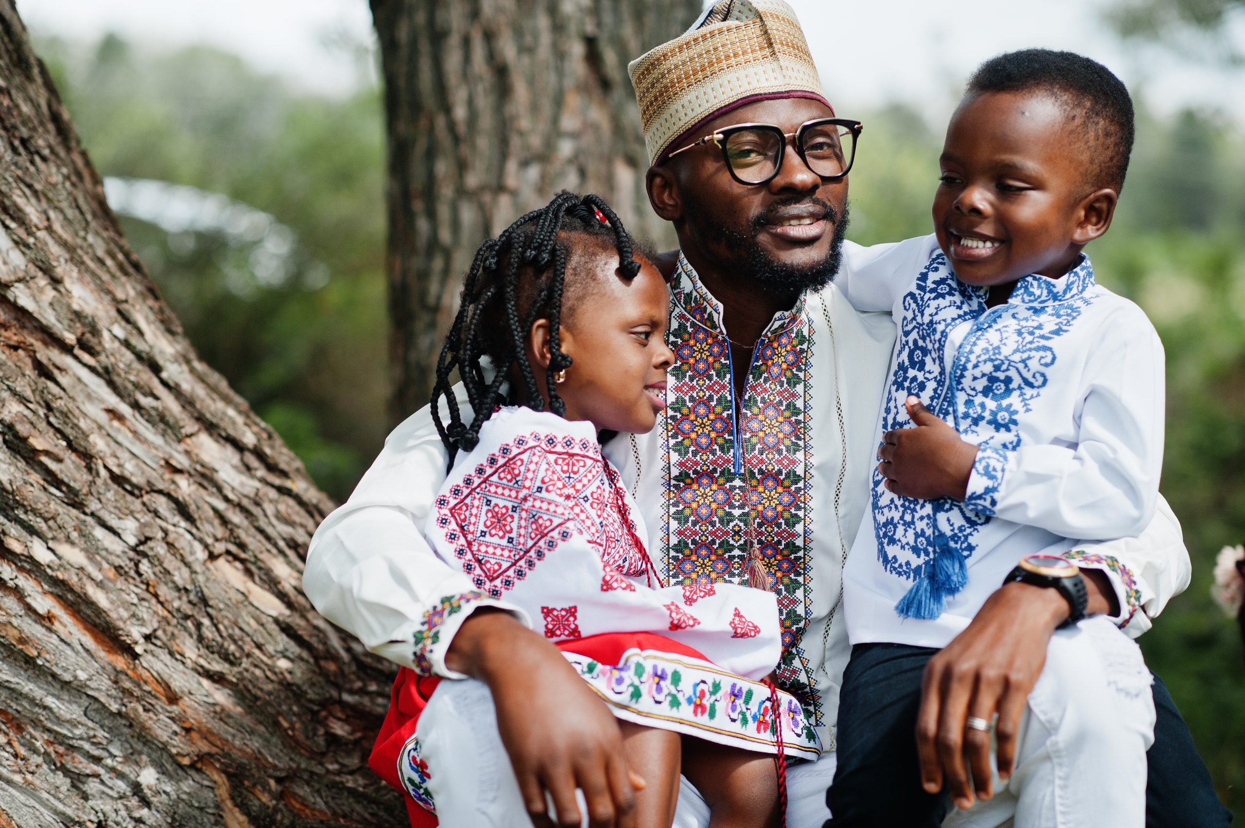African father with kids in traditional clothes at park.