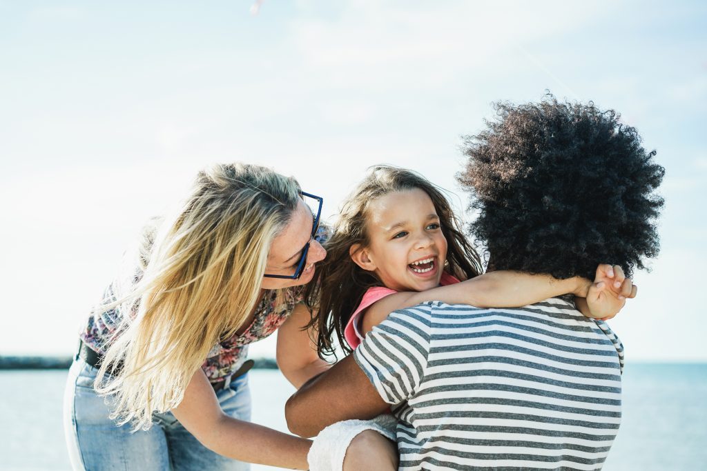 Happy family having fun on the beach - Multi-ethnic couple playing with cheerful daughter on summer time - Focus on kid face