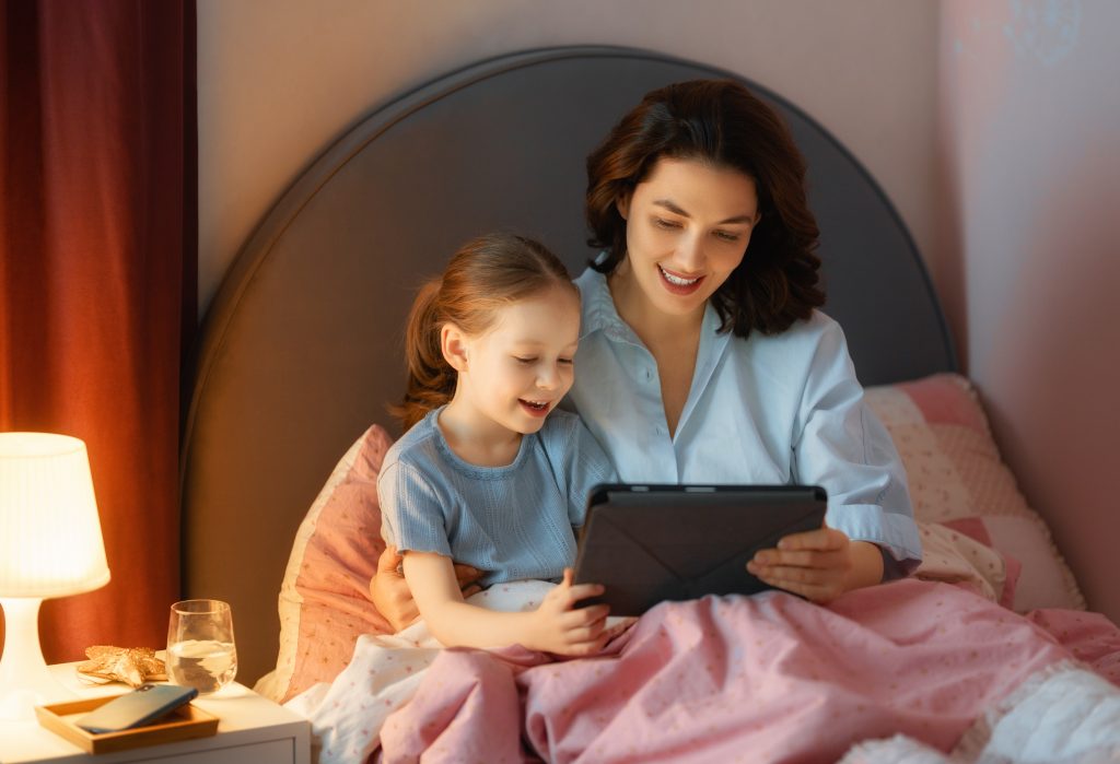 Happy loving family. Young mother and daughter girl using tablet pc. Funny mom and lovely child are having fun at home.