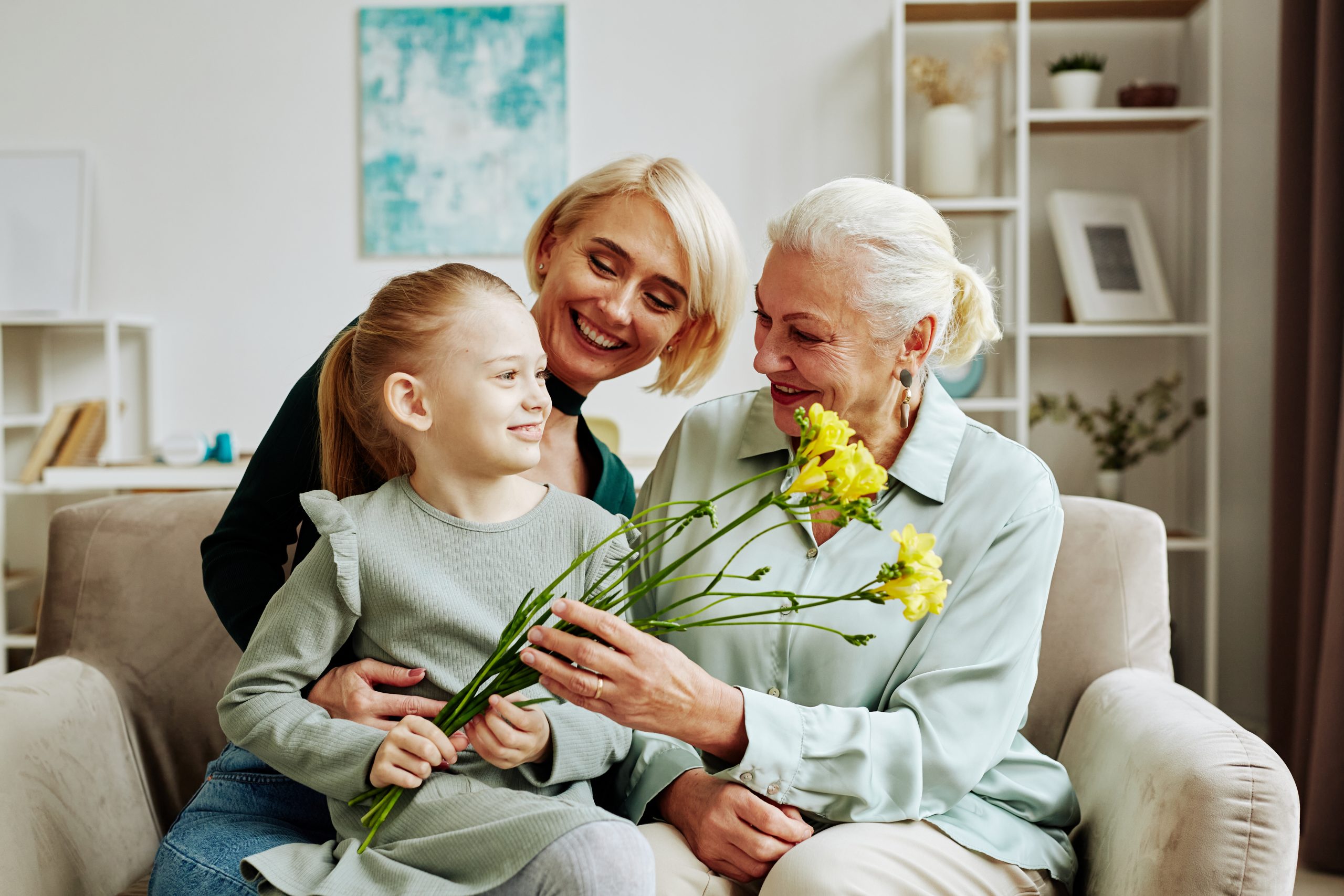Portrait of smiling little girl giving flowers to grandmother on Mothers day in cozy home scene
